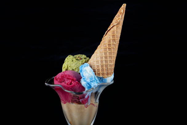 Fruit ice cream scoops overhead on a cornet, served with several colorful spoons isolated on black background. - Foto, imagen