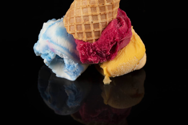 Frutas de sorvete scoops sobrecarga em uma corneta, servido com várias colheres coloridas isoladas em fundo preto. - Foto, Imagem