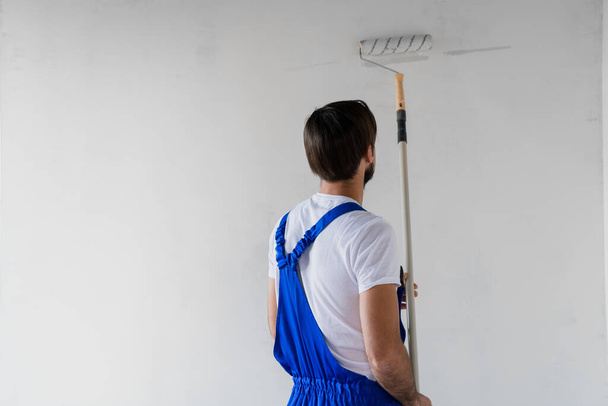 Строитель в синих комбинезонах, рисующий стену веревкой, вид сзади - Фото, изображение
