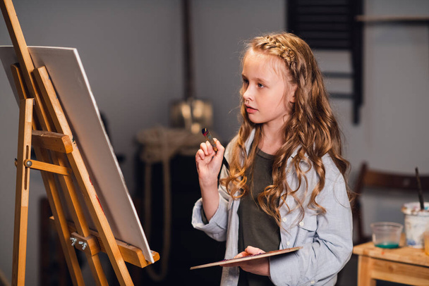 Fiatal lány kreatív művész egy műhelyben. Szenvedéllyel rajzol egy képet a munkába merülve.. - Fotó, kép