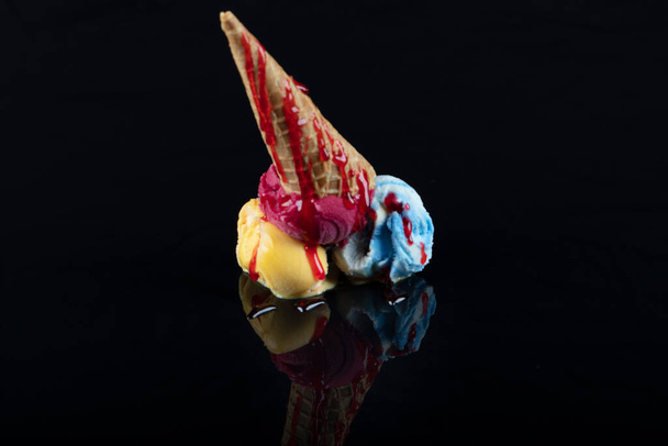 Gelato di frutta scoop in testa su una cornetta, servita con diversi cucchiai colorati isolati su sfondo nero. - Foto, immagini