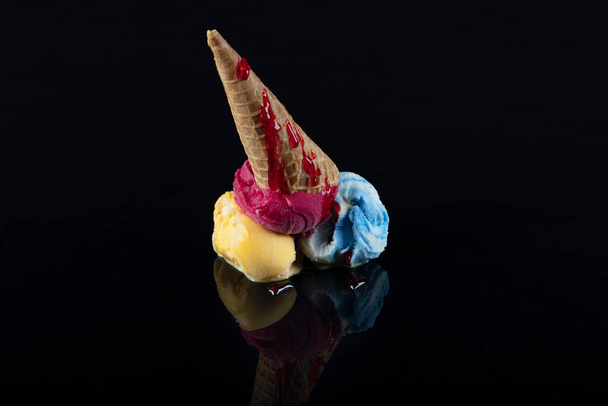 Fruit ice cream scoops overhead on a cornet, served with several colorful spoons isolated on black background. - Photo, Image