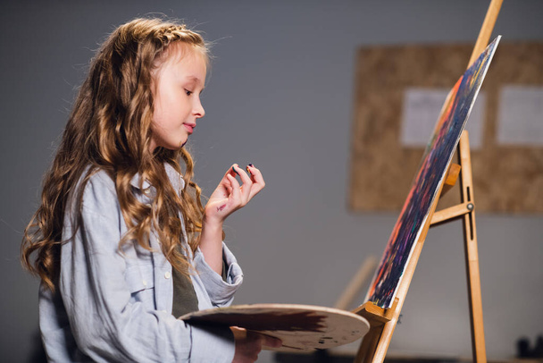 Una estudiante de arte mezcla colores en una paleta para dibujar su lienzo en un taller. - Foto, imagen