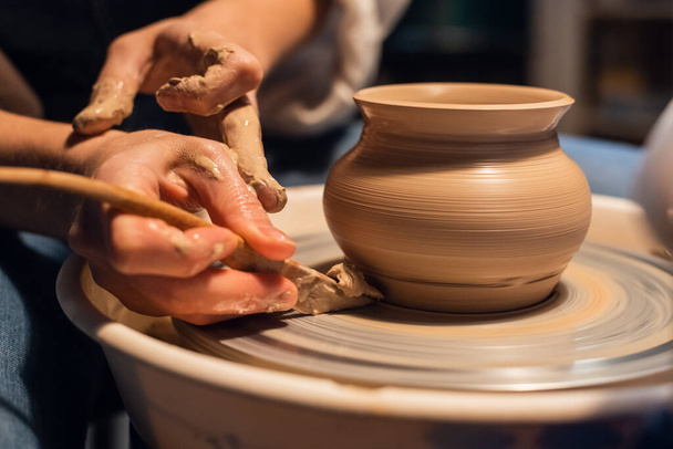 mooie handen van een jong meisje pottenbakker in het proces van beeldhouwen van een vaas met klei en gereedschappen. - Foto, afbeelding
