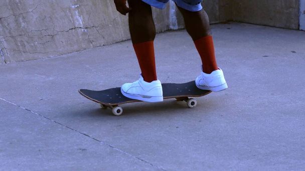 Μια φωτογραφία από τα πόδια ενός μαύρου πάνω σε ένα σκέιτμπορντ. - Φωτογραφία, εικόνα