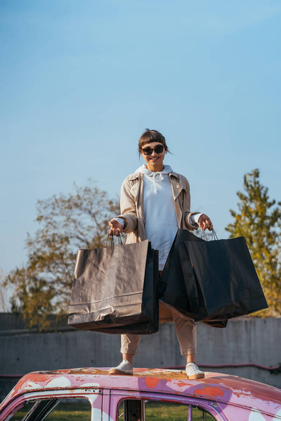 Uma jovem mulher está de pé em um carro com sacos nas mãos - Foto, Imagem