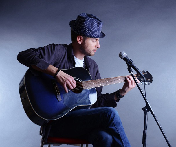 Young musician playing acoustic guitar and singing, on gray background - Photo, image