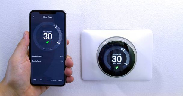 Calgary, Alberta, Canada. Aug. 29, 2020. A person saving energy with a iPhone 11 Pro Max using the nest app on celsius metrics using a wireless Nest Learning Thermostat on a white wall. - Photo, Image
