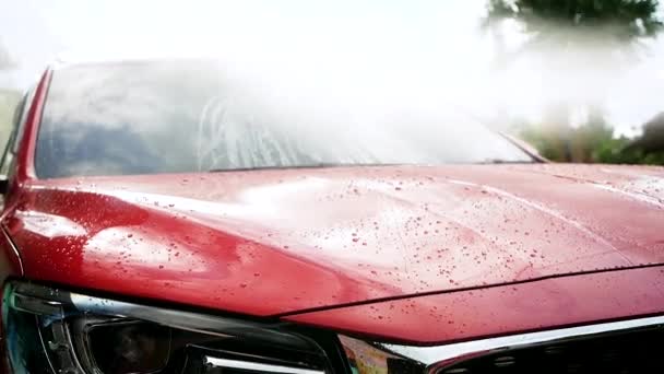 Zbliżenie kropel wody płynącej na samochód podczas pracy przy użyciu wysokociśnieniowego spryskiwacza wodnego myjącego samochód. - Materiał filmowy, wideo