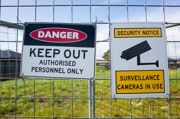 The sign of 'Danger Keep Out Authorised Personnel Only' and ' Security notice Surveillance cameras in use' on a metal construction barrier by a lot of private vacant land. Concept of no trespassing. - Photo, Image