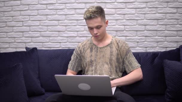 Nuori houkutteleva mies freelancer käyttäen kannettavaa tietokonetta, etätyötä ja opiskelua - Materiaali, video