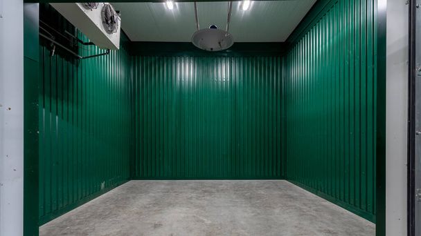 Innenraum der Lagerhalle aus grünem Metallprofil mit Betonboden und Klimaanlage, Industrieschuppen oder Parkplatz. - Foto, Bild