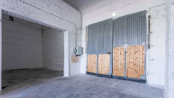 Intérieur du bâtiment industriel avec murs en briques blanches, sol en béton, portes hautes et espace vide pour l'affichage des produits ou arrière-plan industriel - Photo, image