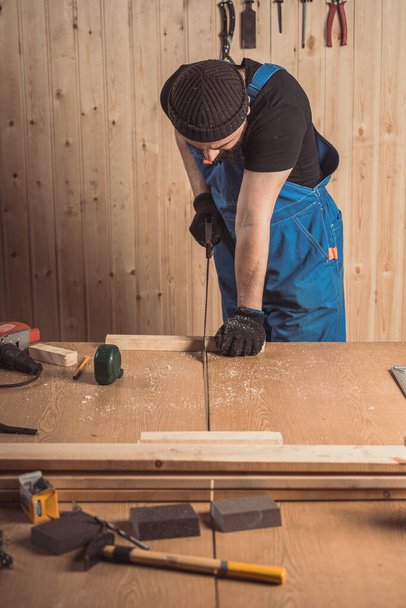 Nahaufnahme eines Mannes, der in der Werkstatt ein Brett mit einer Säge zersägt. Bau- und Wohnungsrenovierung, Reparatur und Bauwerkzeug - Foto, Bild