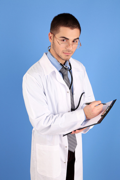Male Doctor standing with folder, on blue background - Фото, изображение
