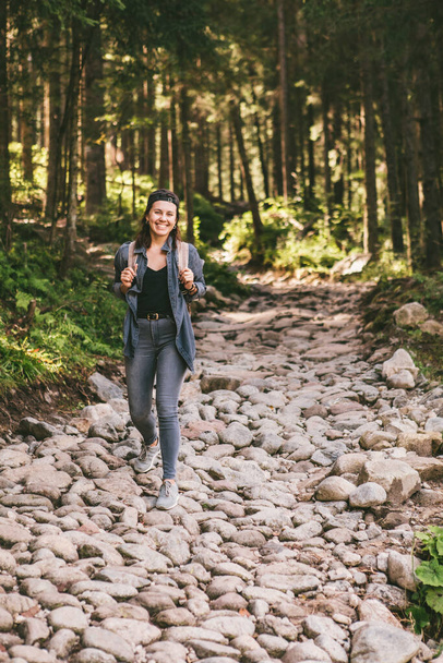 woman with backpack hiking in forest by stone path trail travel concept - 写真・画像