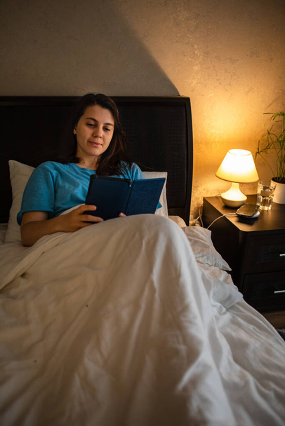 молодая женщина читает электронную книгу с ночной лампой. копировальное пространство - Фото, изображение