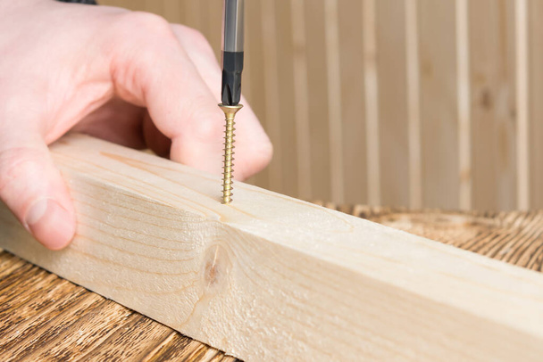 hands hold a wooden block and screw into it a screw with a screwdriver, closeup - Foto, Bild