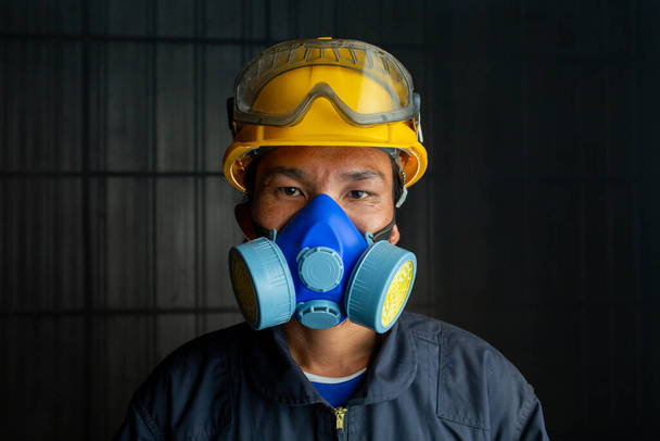 Ασιάτης εργάτης φοράει αναπνευστήρα σε καπνιστή, τοξική ατμόσφαιρα. Η εικόνα δείχνει τη σημασία της ετοιμότητας προστασίας και της ασφάλειας στο βιομηχανικό εργοστάσιο. - Φωτογραφία, εικόνα