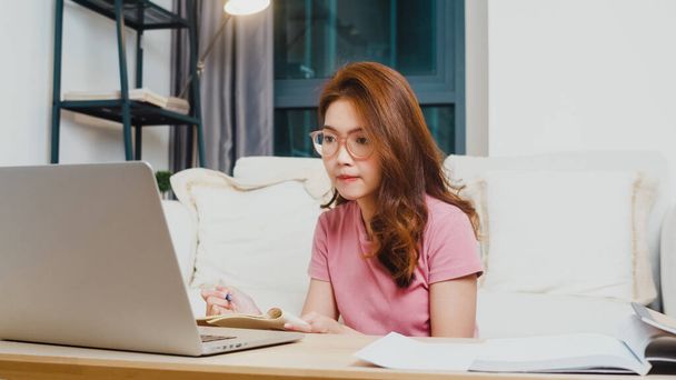 Fiatal ázsiai tini lány diák távolság tanulás lecke online tanár és tanulmány a számítógép laptop a nappaliban otthonról éjszaka. Társadalmi távolság, karantén a koronavírus megelőzése érdekében. - Fotó, kép