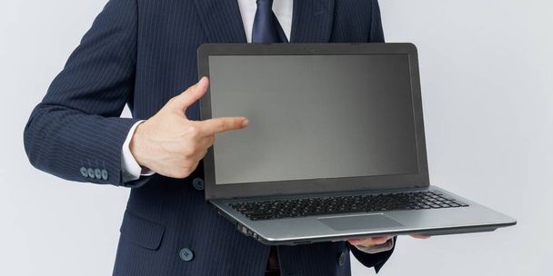 A businessman holds a laptop, the other hand shows the screen. White background. No face visible. Business and finance concept - Zdjęcie, obraz