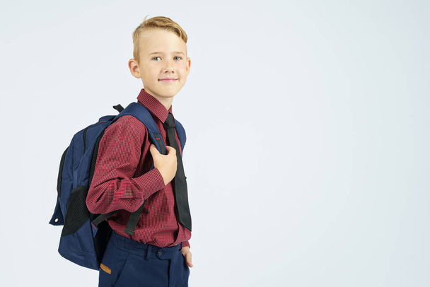 A schoolboy holds a school backpack, stands sideways, looks at the camera. Education concept - Foto, imagen