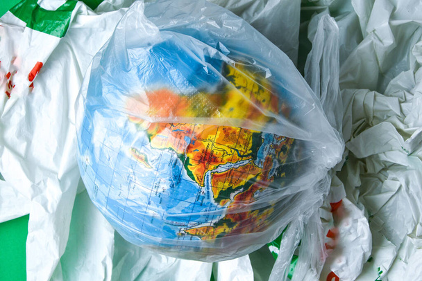 globe is in a plastic bagon trash. concept of plastic pollution of the earth. World Environment Day concept.Toy world globe in white plastic bag. Copy space for text. Save Earth - Photo, Image