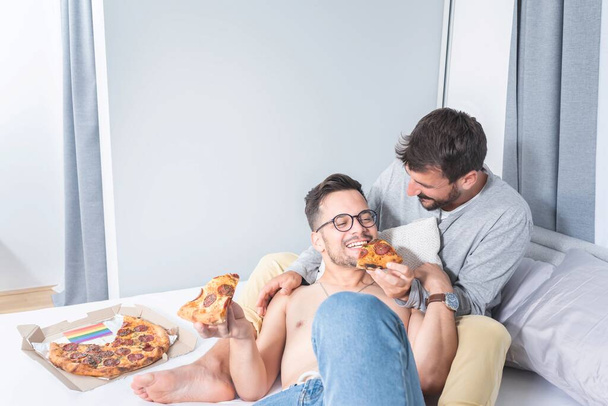 Gay couple eating pizza on bed at home - Foto, imagen