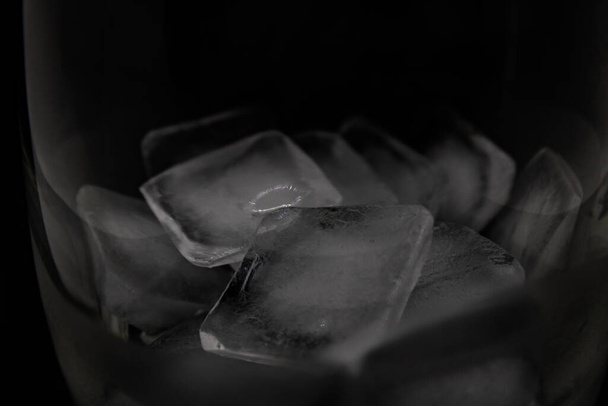 Glass with melting ice cubes close up on a black background - Fotografie, Obrázek