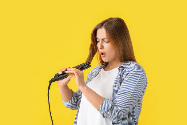 Stressed woman with straightening iron on color background - Foto, immagini