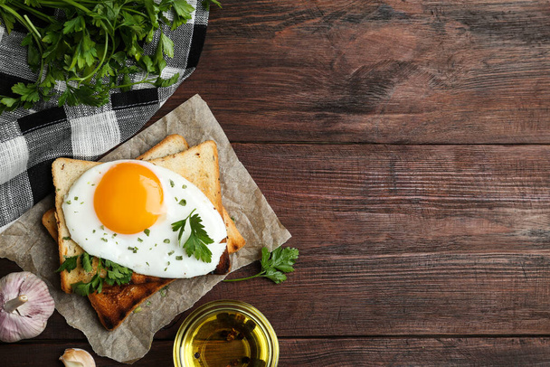 Tasty fried egg with toasts and parsley on wooden table, flat lay. Space for text - Foto, afbeelding