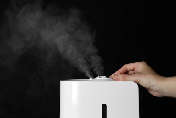 Woman using modern air humidifier on black background, closeup - Photo, Image