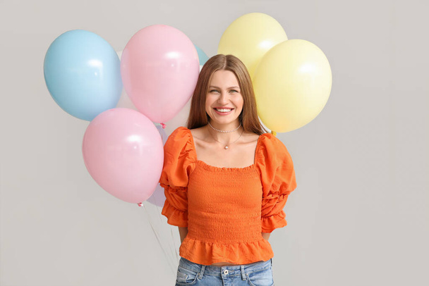 Young woman with balloons on grey background - Foto, afbeelding