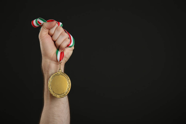 Man holding golden medal on black background, closeup. Space for design - Zdjęcie, obraz