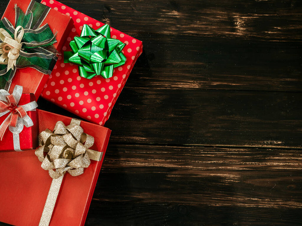 Χριστούγεννα και ευτυχισμένο το νέο έτος φόντο. Κάτοψη του όμορφου κόκκινου κουτιού δώρου με γυαλιστερό πράσινο και χρυσό φιόγκο διακοσμήσεις σε σκούρο ξύλινο σανίδι φόντο με αντίγραφο χώρου. - Φωτογραφία, εικόνα