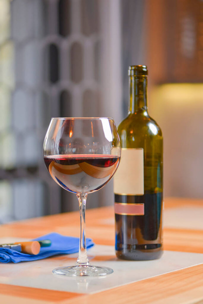 Wine glass and bottle of red wine on a wooden table over blurred background. Restaurant service, eating out concept. Drinking alcohol in a restaurant, celebration. - Photo, image