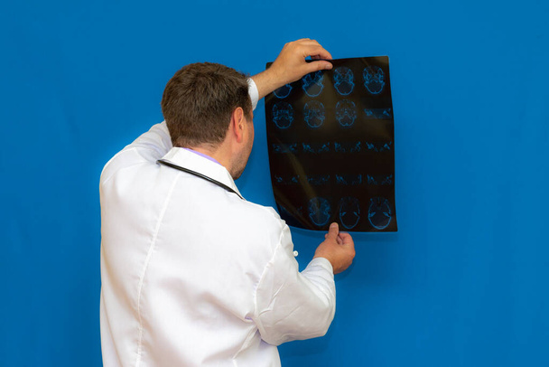 Przemyślany kaukaski lekarz neurologiczny oglądający tomografię mózgu na niebieskim tle. Braing Imaginning zbadane przez młodego lekarza. - Zdjęcie, obraz