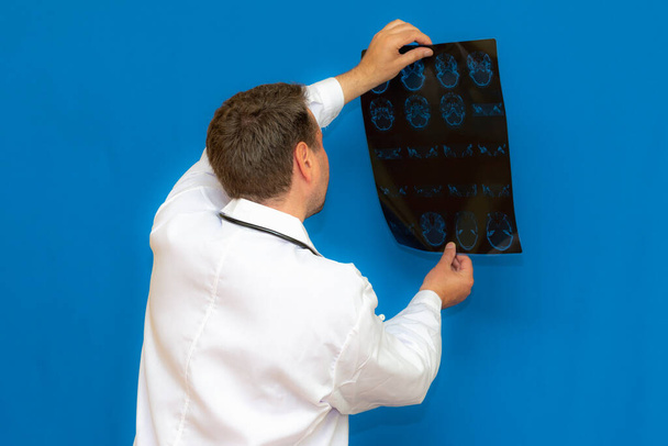 青い背景に脳CTスキャンを見る思慮深い原因アジアの神経内科医。若い医師によって検査された脳の想像力. - 写真・画像