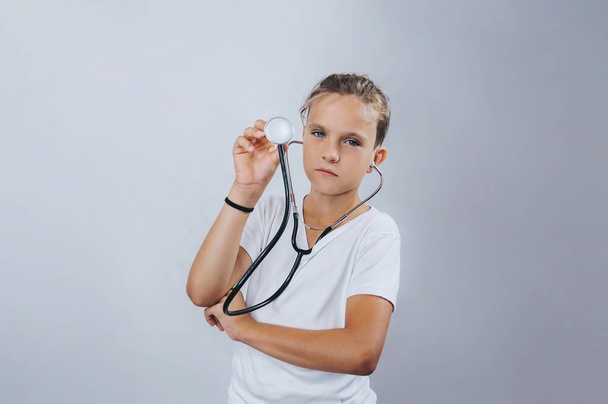 Boy holding a stethoscope in his hands on an isolated light background. Medical education, choice of profession, future. Caucasian, handsome. - Фото, изображение