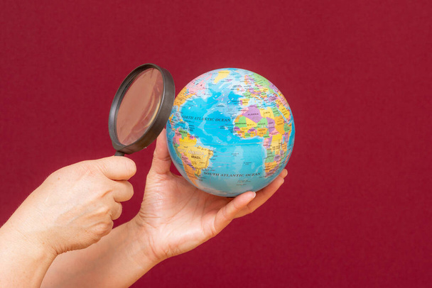 Conceptual image of a hand holding a magnifying glass over an world globe - Photo, Image