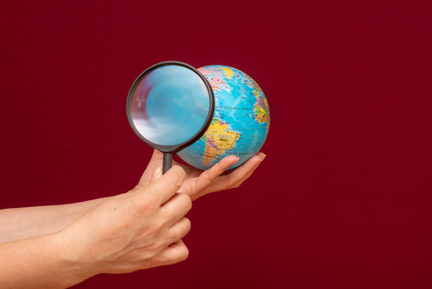 Conceptuele afbeelding van een hand die een vergrootglas over een wereldbol houdt - Foto, afbeelding