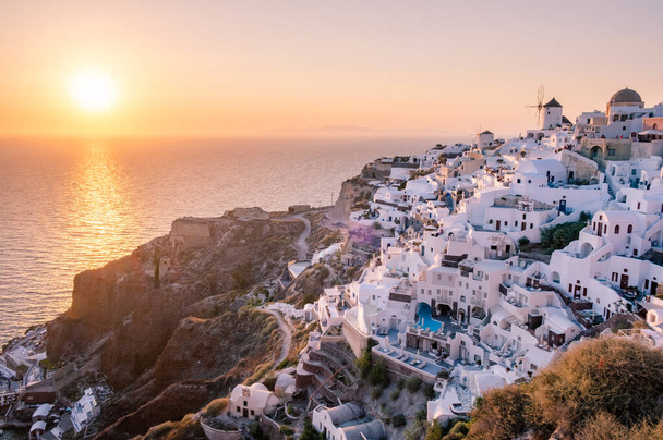 サントリーニ島の夕日ギリシャ,日没の間に教会や風車と美しい白塗りの村Oia - 写真・画像