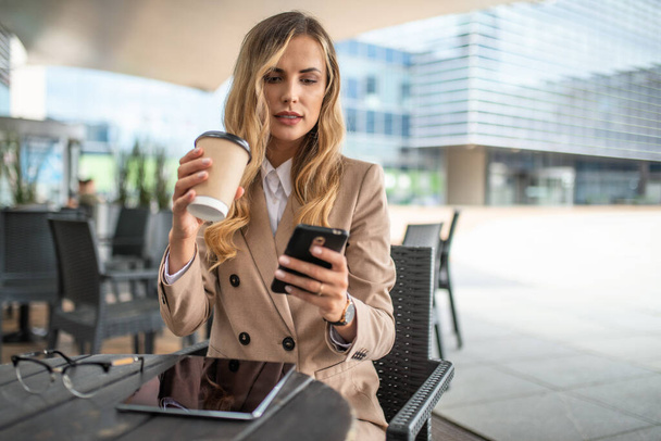 Young blonde businesswoman on a coffee break using her smartphone - 写真・画像