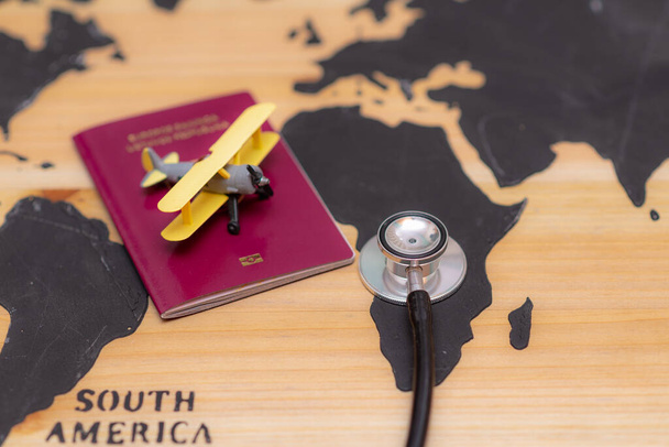 Visão superior do conceito de viagem médica com documento de passaporte estetoscópio e avião de brinquedo no fundo do mapa mundial de madeira. - Foto, Imagem