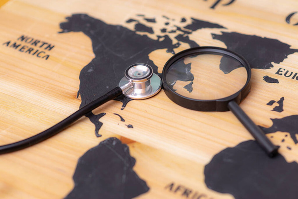Stethoscope and magnifying glass on wooden world map background. Selective focus. - Photo, Image