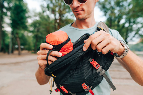 Turista masculino pone una bolsa con una hamaca en una bolsa de cintura. Concepto de equipo de camping. Cerrar foto - Foto, imagen