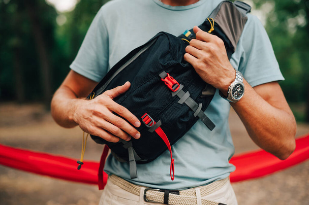 Feche a foto recortada de um saco de cintura para viajar no ombro de um jovem na floresta. Equipamento para turismo. - Foto, Imagem