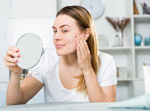 Cheerful woman is concentrared looking on her face in the mirror - Photo, image