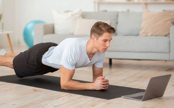 Фітнес-тренування, статичні вправи. М'язистий чоловік з ноутбуком робить дошку і дивиться онлайн урок
 - Фото, зображення