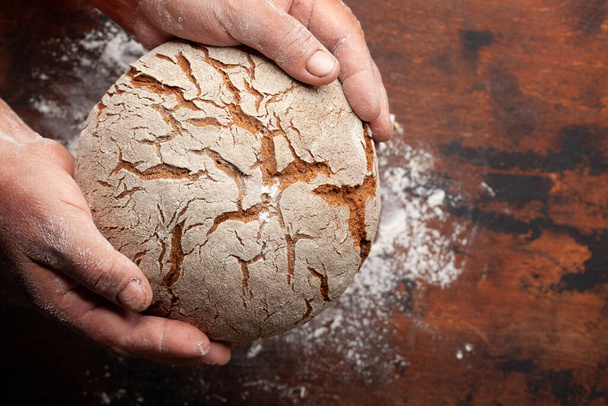 Bäcker mit frisch gebackenem selbstgebackenem Brot in der Hand auf einem Holztisch. Draufsicht flach lag mit Kopierraum - Foto, Bild